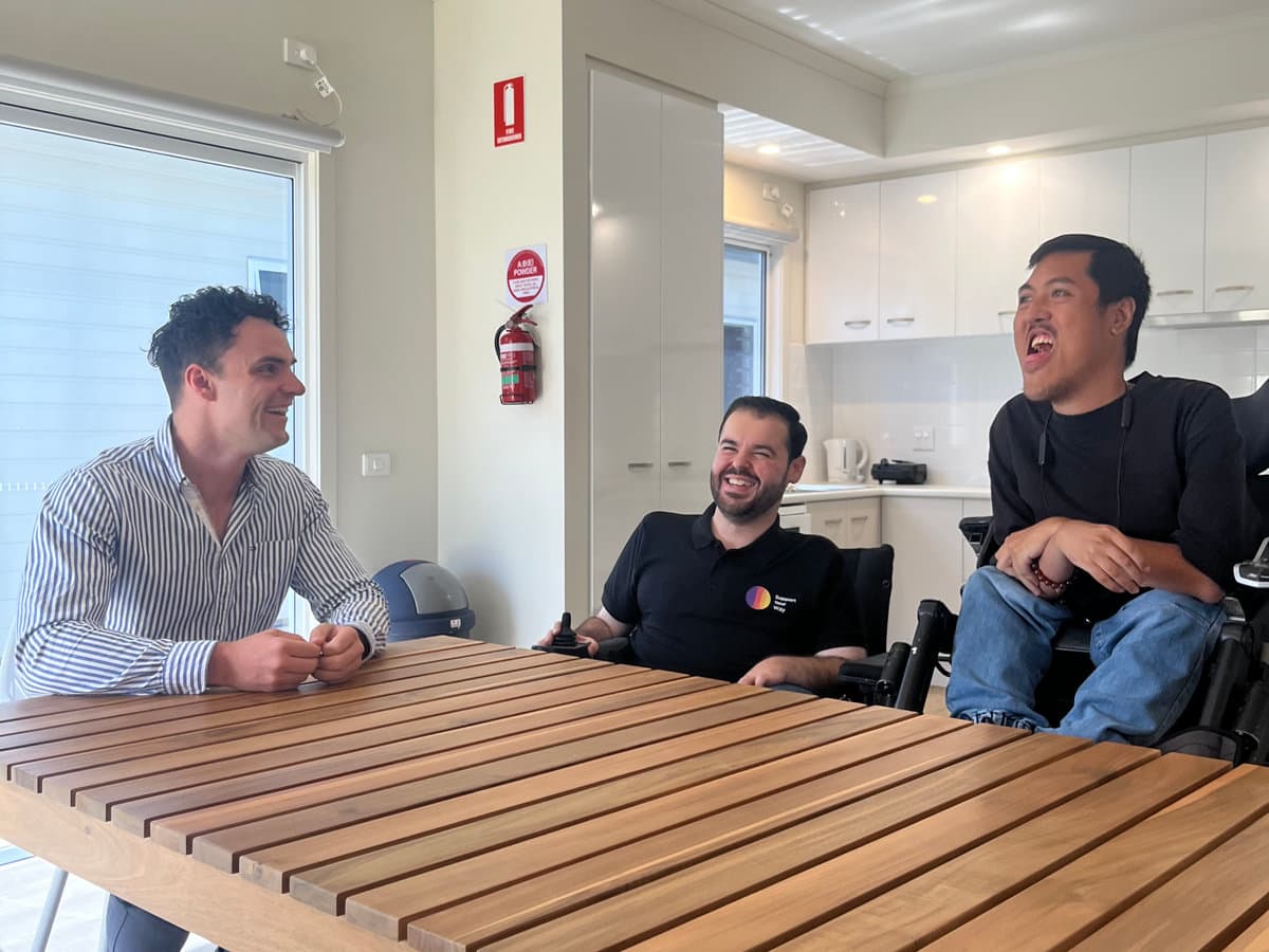 Participants and support worker sharing laughter and conversation around a bright dining table in Sydney
