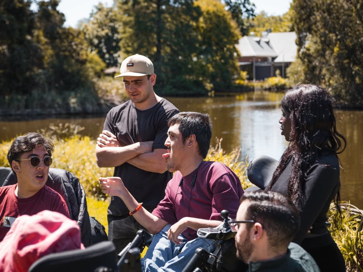 A diverse group of support workers and participants enjoying an afternoon gathering in a sunny park